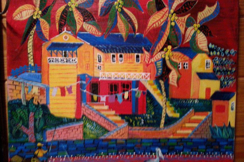 Case créole colorée aux Antilles avec cocotiers linge séchant et pélican au bord de l'eau